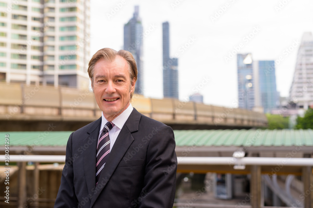 Happy mature handsome businessman in suit smiling at the skytrain station Happy mature handsome businessman in suit smiling at the skytrain station