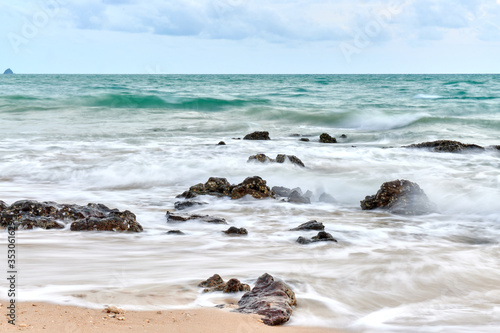a wavy sea with rocks near a beach.