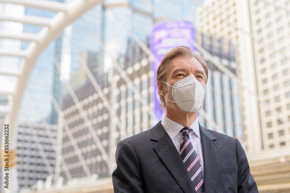 Mature businessman with mask for protection from corona virus outbreak thinking at skywalk bridge