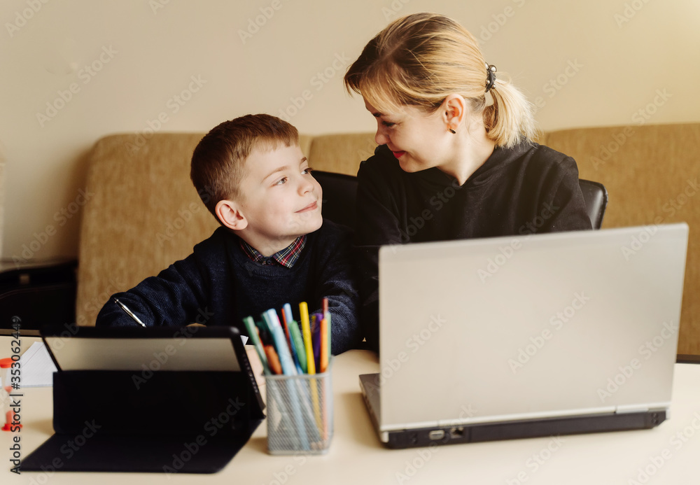 Mother using laptop and tablet teaching with her son online at home in his room Mother using laptop and tablet teaching with her son online at home in his room