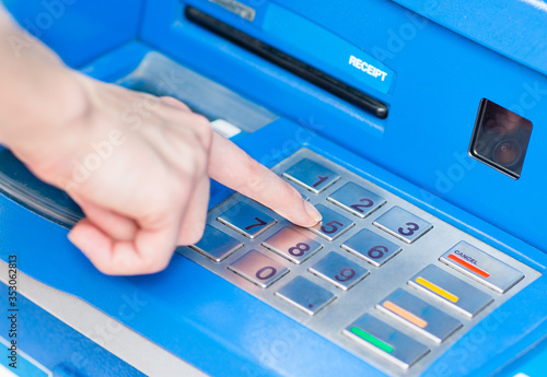 Closeup of caucasian person's hand entering PIN code on blue ATM bank machine keypad. 