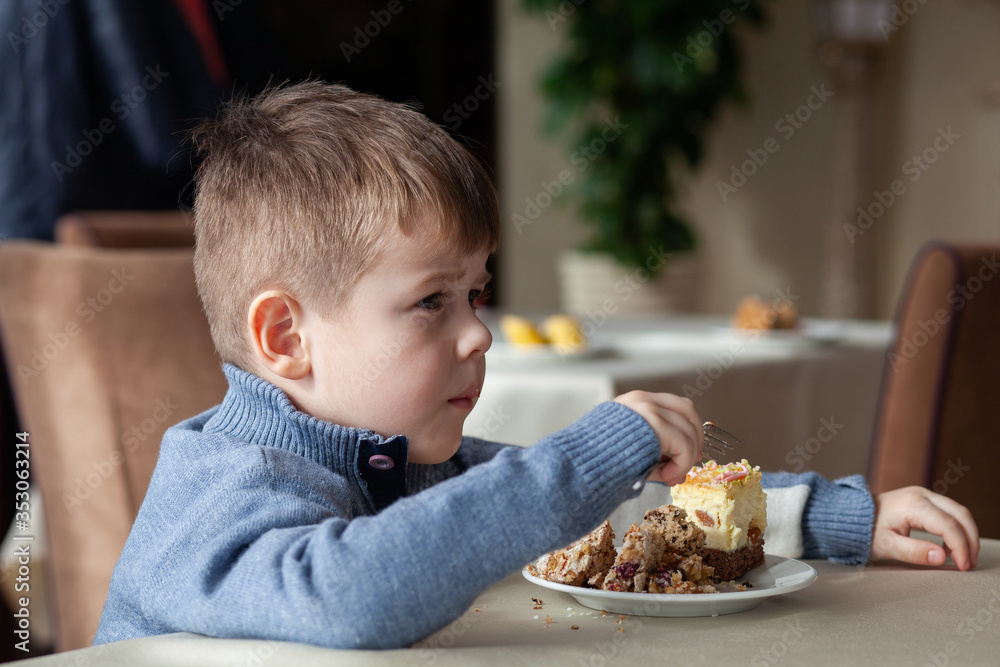 Cute little boy in cafe eat a big piece of cake with a fork. Desserts for kids. Cute little boy in cafe eat a big piece of cake with a fork. Desserts for kids.