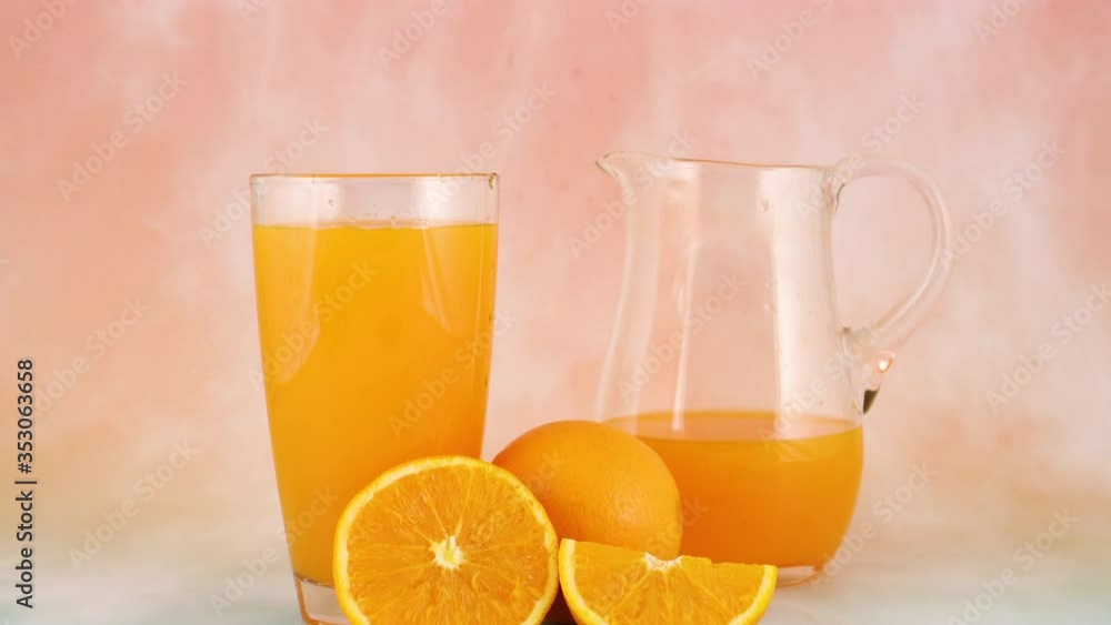 Fresh squeezed orange juice in glass and jug on pastel background with sliced orange Fresh squeezed orange juice in glass and jug on pastel background with sliced orange
