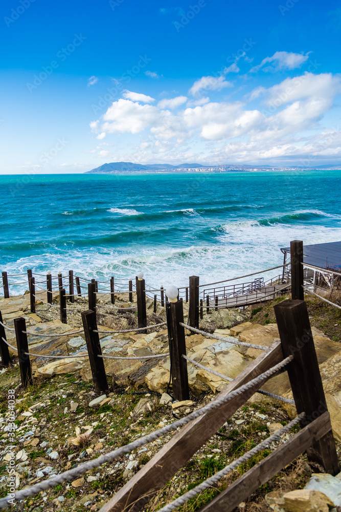 A staircase with stone steps and rope handrails leads down to the green stormy sea. On the horizon mountains and ships on the roadstead of Novorossiysk A staircase with stone steps and rope handrails leads down to the green stormy sea. On the horizon mountains and ships on the roadstead of Novorossiysk