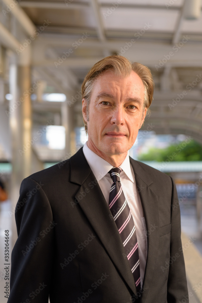 Naklejka premium Mature handsome businessman in suit at footbridge in the city