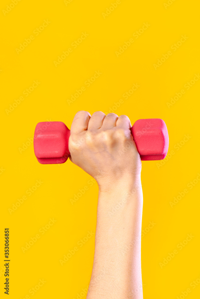 Woman hand holding pink dumbbell isolated on yellow
