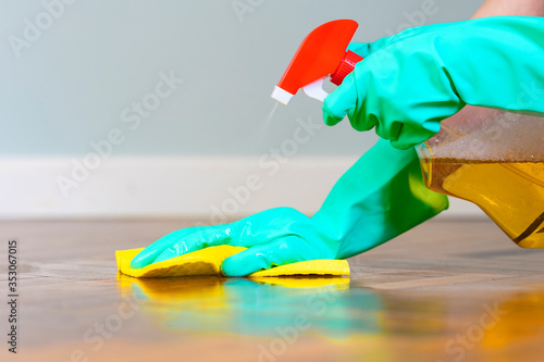Female hands with rubber gloves cleaning parquet with detergent and cloth