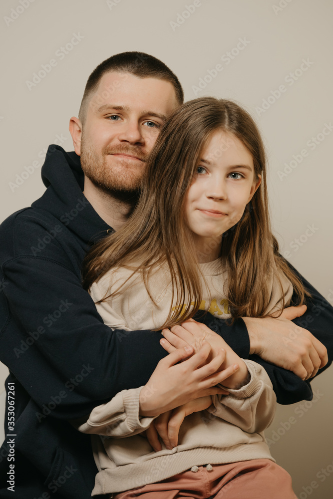 A young happy father with a beard hugs strongly his cute daughter. A child with long hair sitting on daddy's lap. Family photo. A young happy father with a beard hugs strongly his cute daughter. A child with long hair sitting on daddy's lap. Family photo.
