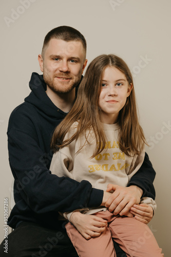 A young happy father with a beard hugs strongly his cute daughter. A girl with a smile sitting on daddy's lap. Family photo.