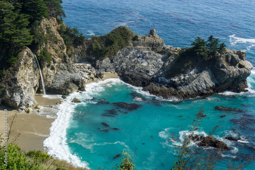 Coastal waterfall cascading onto Pacific white sand beach surrounded by rocky cliffs
