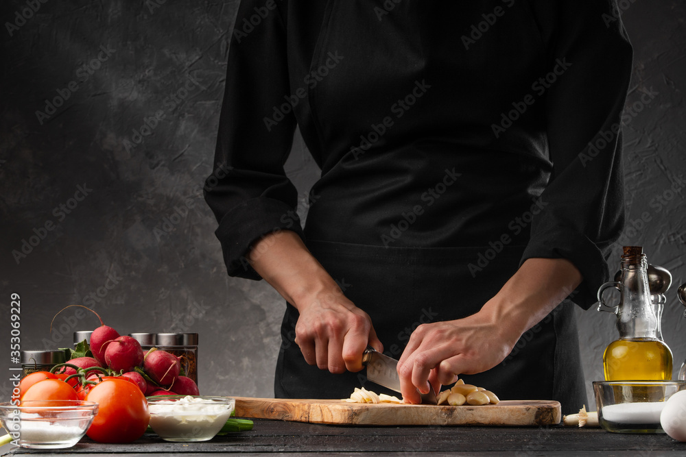 Chef chopping garlic for cooking. Against the background of a gray wall, and vegetables. Cooking and recipe book.