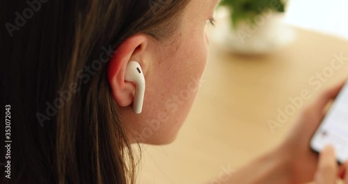 Woman inserts a wireless white earphone into her ear close-up