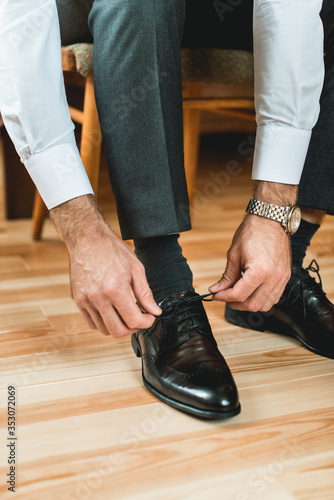 Man ties his shiney new black leather shoes.