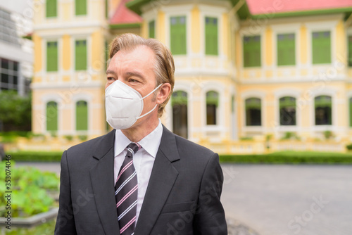 Face of mature businessman with mask for protection from corona virus outbreak thinking in the city outdoors