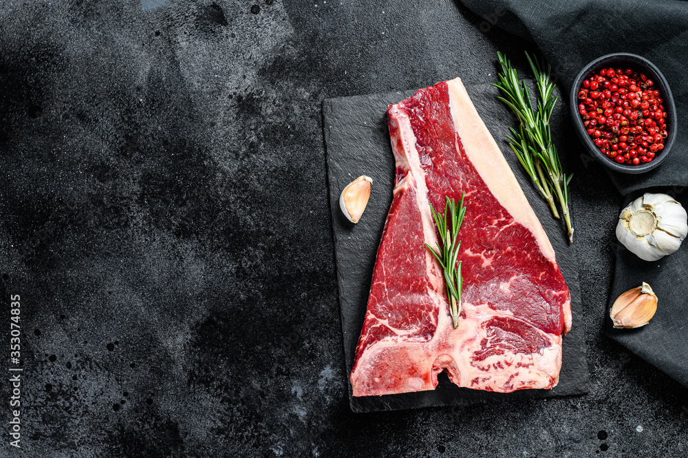 Raw fresh meat t-bone steak with spices, garlic and rosemary. Organic t bone beef. Black background. Top view. Copy space