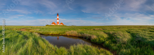 Stunning,  idyllic panorama view of the Westerheversand Lighthouse and salt meadows landscape at Westerhever by evenning sunshine with blue cloudy sky, Nordfriesland, German state of Schleswig-Holstei photo