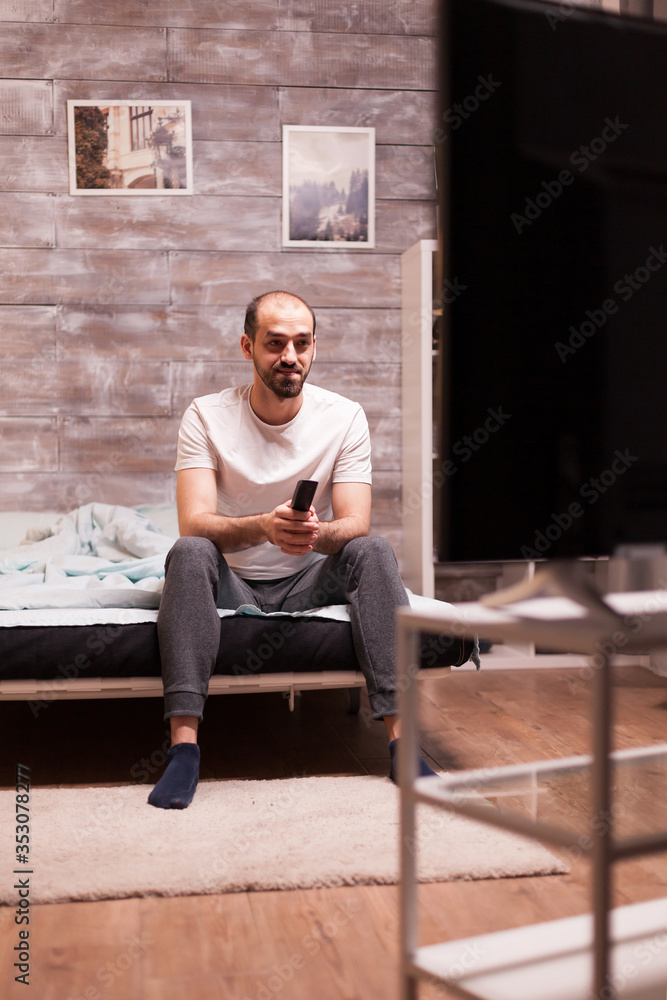 Cheerful man in pajamas at night watching tv holding remote control. Cheerful man in pajamas at night watching tv holding remote control.
