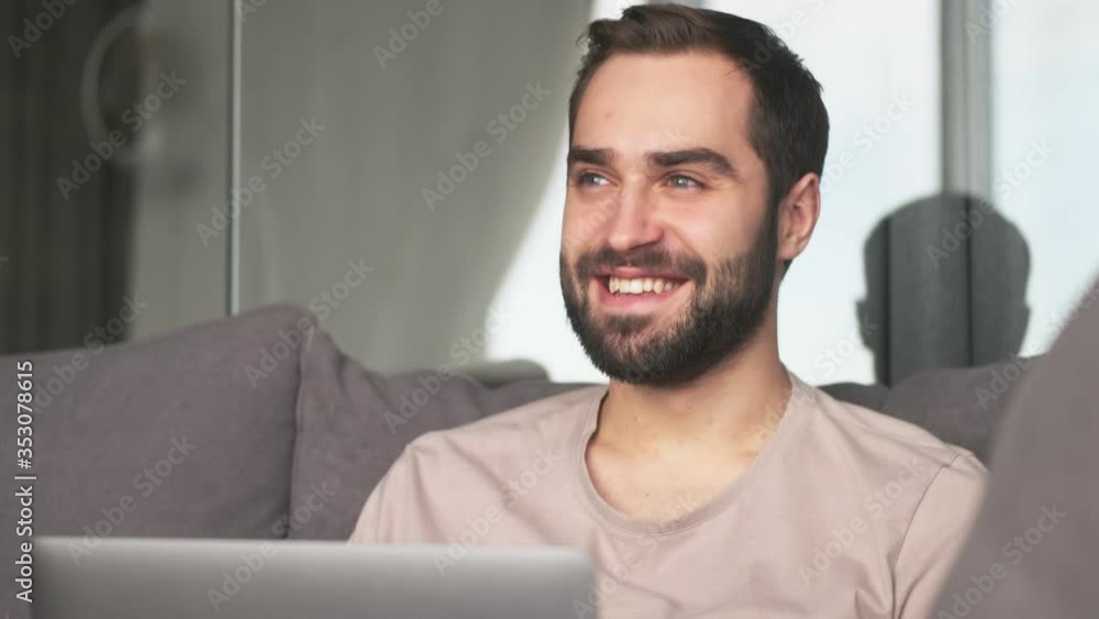A pleased young man is watching something in his laptop sitting at home on the sofa in the living room A pleased young man is watching something in his laptop sitting at home on the sofa in the living room