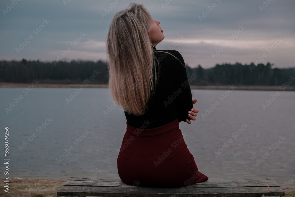 Girl sits on the bank of the river on a cloudy day.