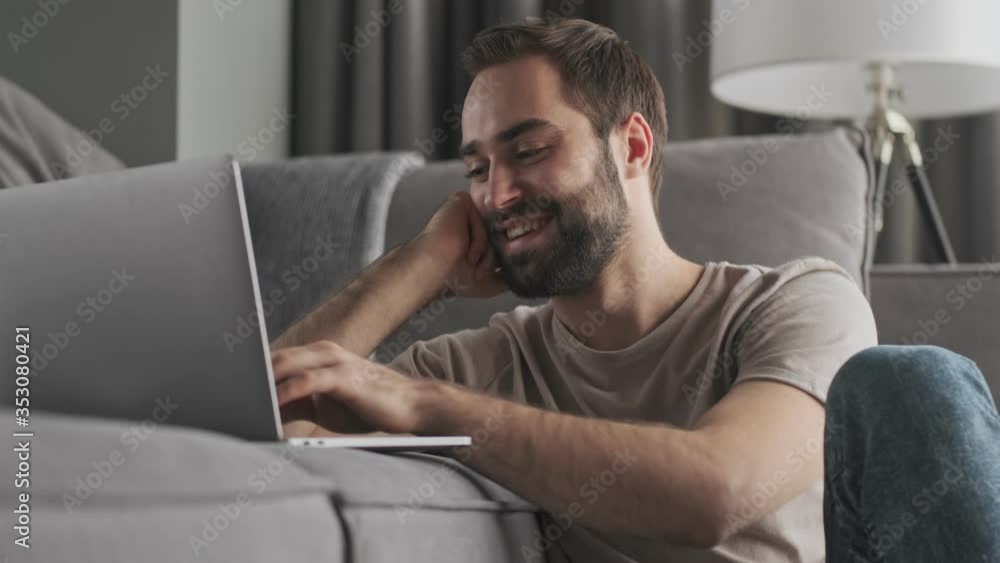 A happy young man is typing on his laptop sitting at home in the living room A happy young man is typing on his laptop sitting at home in the living room