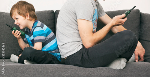 The dad talking with his son by walkie talkie sitting on sofa