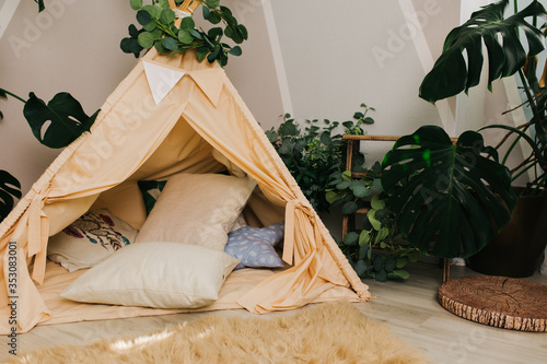 children's room: live tropical plants with large leaves, soft pillows, a teepee. interior elements: wooden inscription 