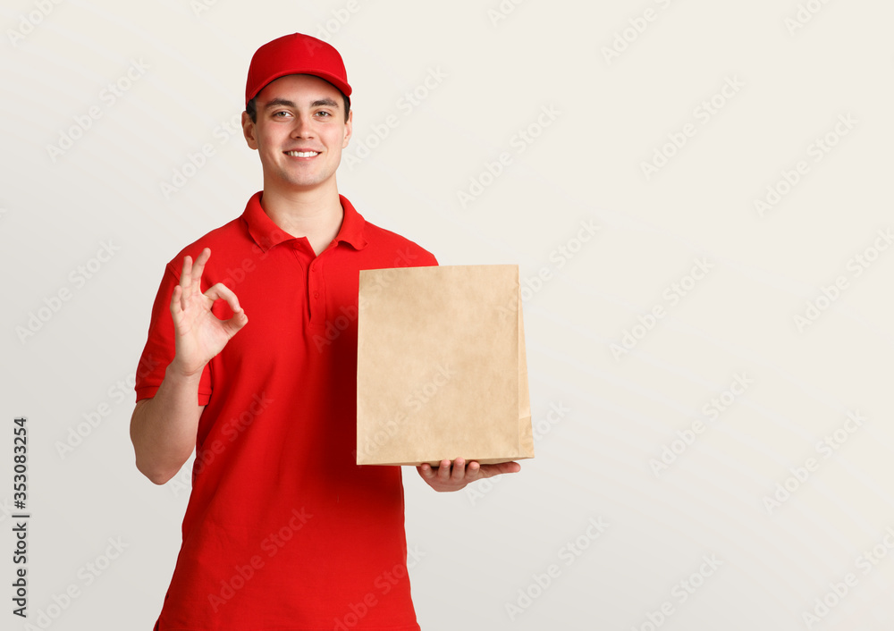 Courier in uniform holds paper package and shows symbol ok with hand Courier in uniform holds paper package and shows symbol ok with hand