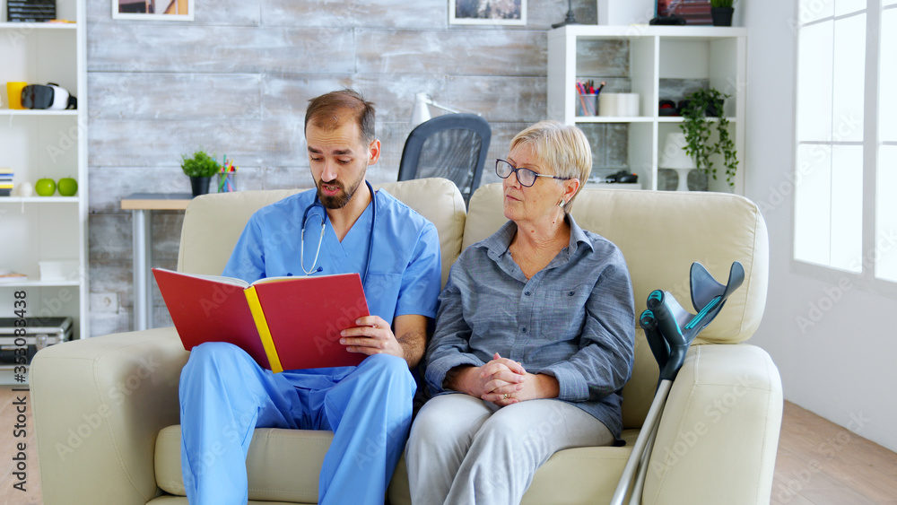 Male assistant in nursing home reading a book to retired elderly pensioner. Caregiver and social worker Male assistant in nursing home reading a book to retired elderly pensioner. Caregiver and social worker