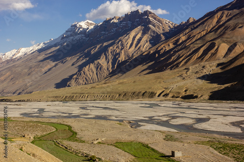 A river flowing between high mountains and green fields of the Spiti Valley