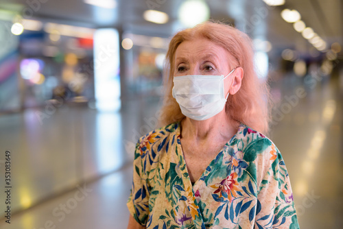 Portrait of blonde senior woman with mask social distancing at subway train station