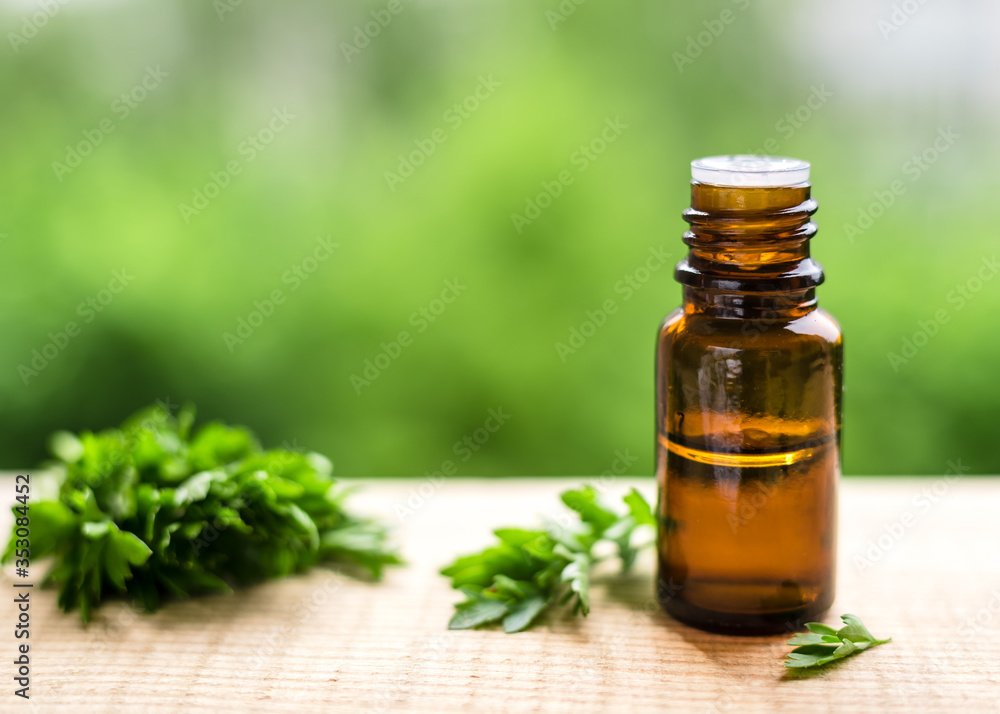 aroma Parsley oil in a dark glass bottle on a wooden table and natural green background aroma Parsley oil in a dark glass bottle on a wooden table and natural green background