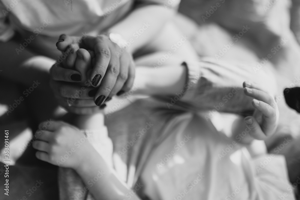 Soft focus. Close up shot of woman hands and her son legs. Young mother holds in her hands the legs of the baby. She is playing with the baby in bed. Black and white photo