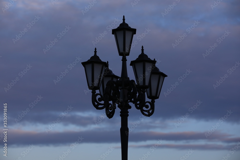 Night image of a street lamp against a purple sky.The silhouette of a forged retro lamp in lilac clouds in the haze.Beautiful evening background.Russia