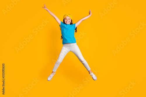 Full length photo of crazy little lady jump high up good mood spread hands legs star shape figure wear casual blue t-shirt headband trousers shoes isolated yellow color background