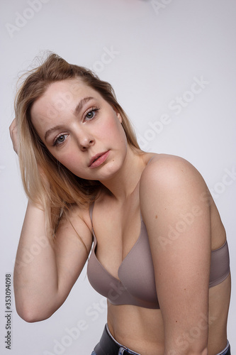 beauty portrait of plump caucasian woman with long blond hair posing in beige lingerie on white studio background. model tests of young girl in bra. attractive female with clean skin