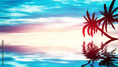Tropical sunset with palm trees and sea. Silhouettes of palm trees on the beach against the sky with clouds. Reflection of palm trees on the water.