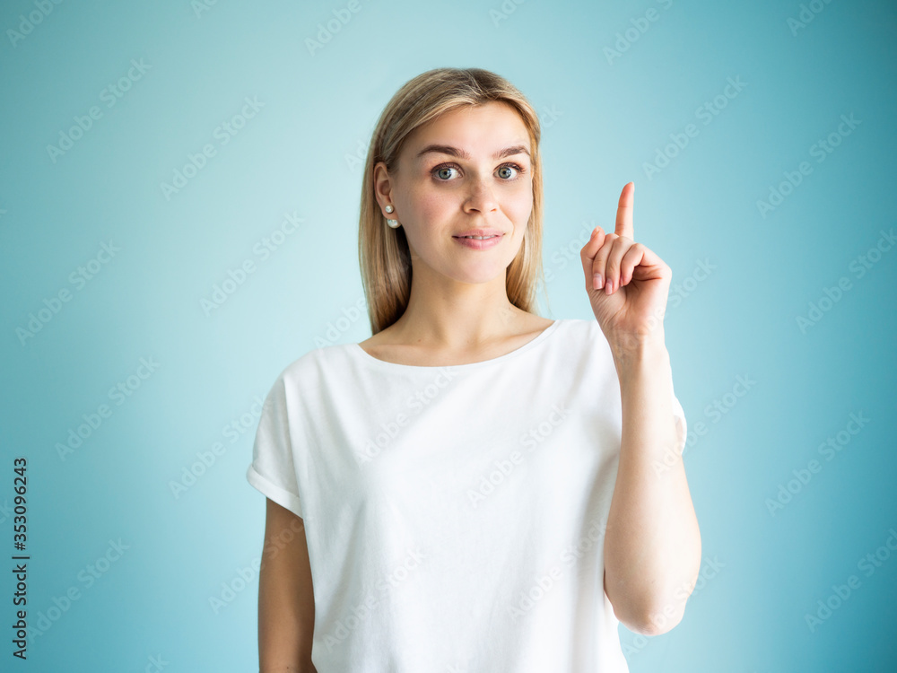 Forefinger points up gesture. Portrait of pretty woman, idea and solution concept on a blue background Forefinger points up gesture. Portrait of pretty woman, idea and solution concept on a blue background