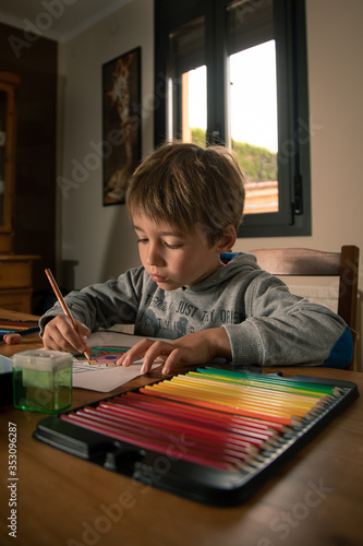 boy painting with wood colors in his house next to a window