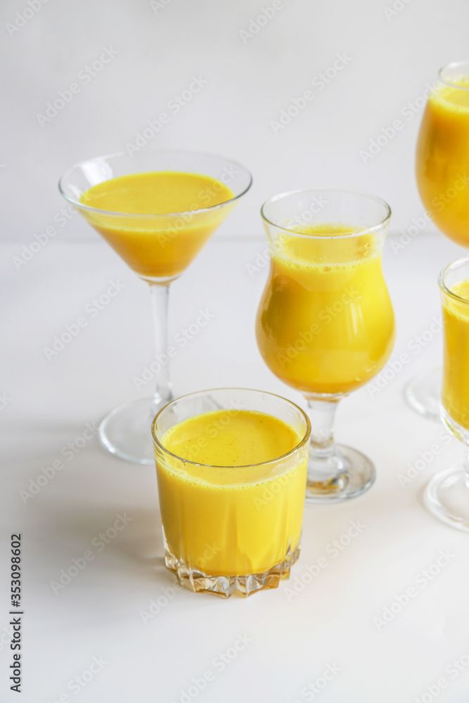 Golden milk with turmeric in different glasses on white background. Healthy spicy curcuma drink concept. Trendy minimal food Golden milk with turmeric in different glasses on white background. Healthy spicy curcuma drink concept. Trendy minimal food