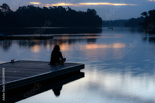 Alone women relax on wooden dock at peaceful lake