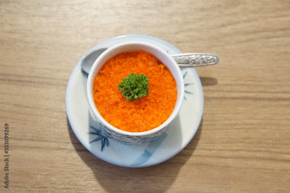 orange Caplin roe Japanese food on top with green vegetable in white cup white plate with spoon on wood background orange Caplin roe Japanese food on top with green vegetable in white cup white plate with spoon on wood background