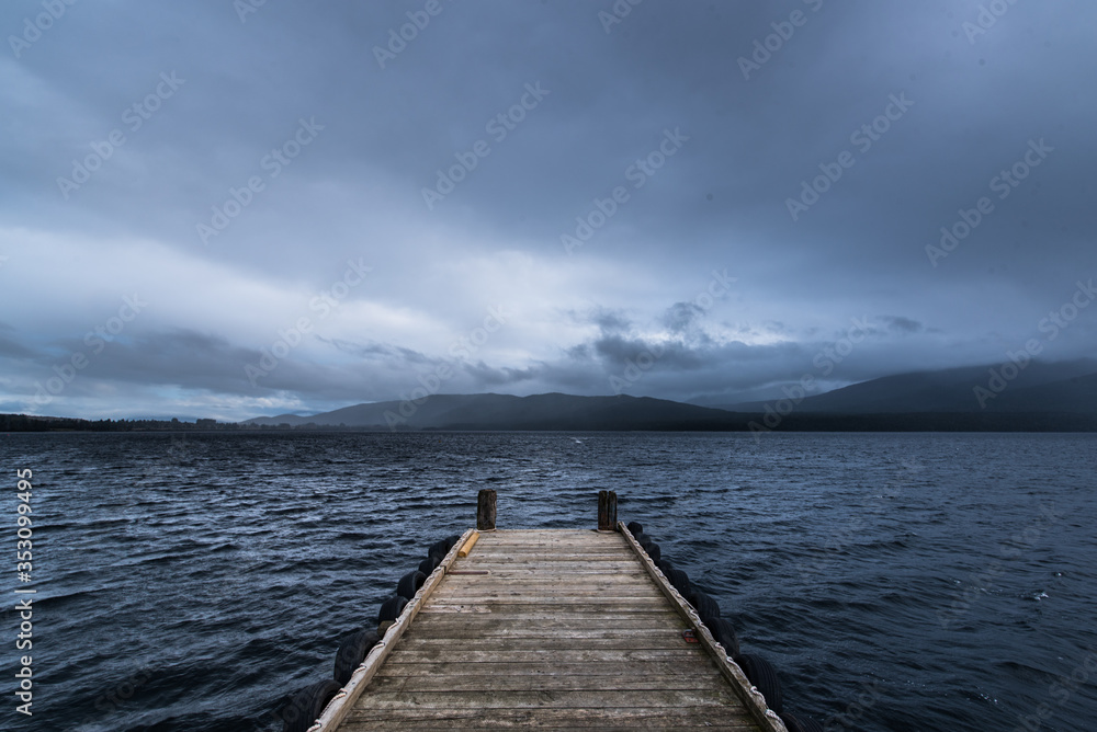 Naklejka premium wooden dock in the lake with raining at mountain background