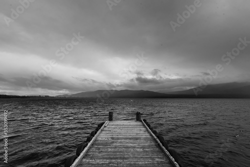 wooden dock in the lake with raining at mountain background, black and white