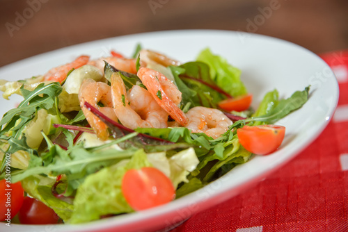 Vegetable salad with shrimp on white plate on red-white tablecloth