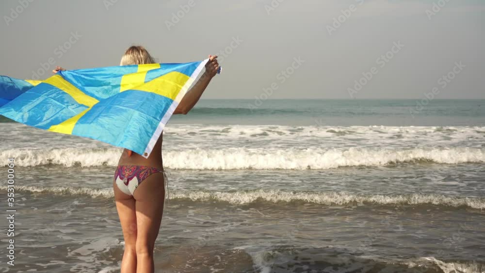 Woman with Sweden flag at sea. Girl with a swedish flag on the beach