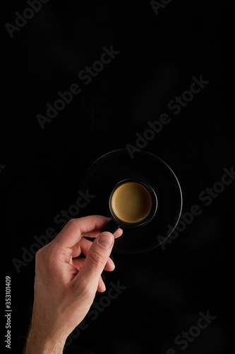 hand holds a black cup with coffee on a black background vertical