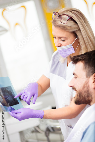 Smiling and happy young female Caucasian dentist showing x-ray images to mail patient after successful medical treatment