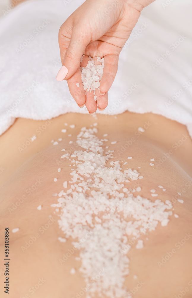 Spa scrub massage. Hands sprinkle salt on back of girl