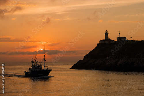 Hermoso atardecer sobre la ría con la silueta del faro sobre la montaña con colores cálidos en las nubes 