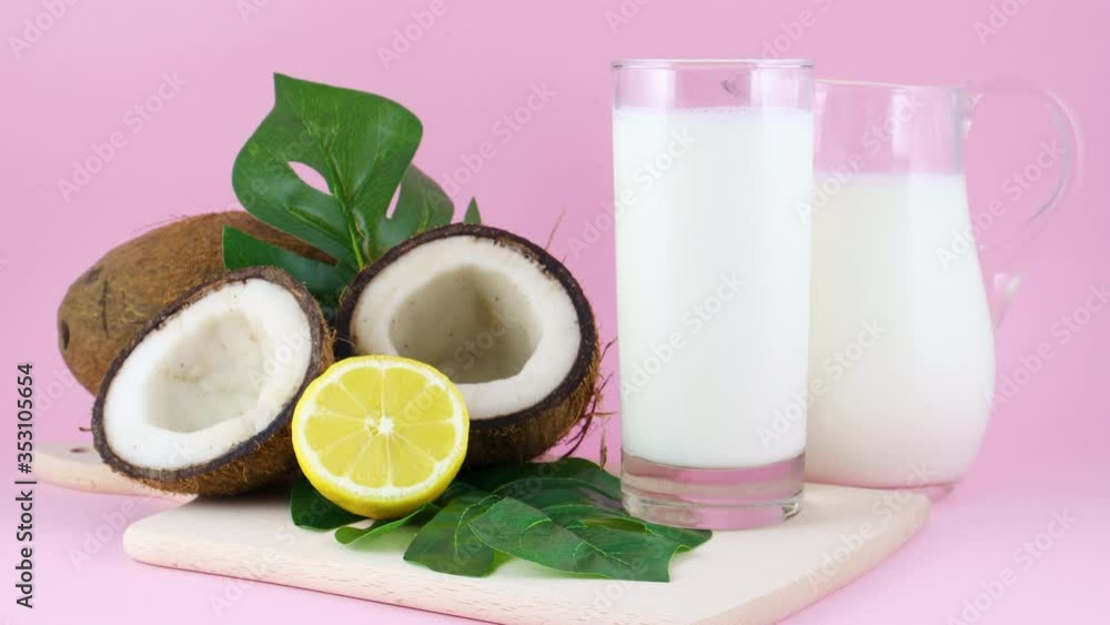 Coconut milk in drinking glass with sliced coconut and lemon on pink background Coconut milk in drinking glass with sliced coconut and lemon on pink background